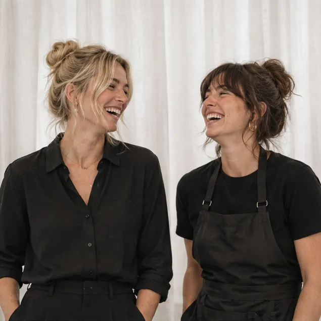 Two SAGE stylists laughing in front of linen curtains